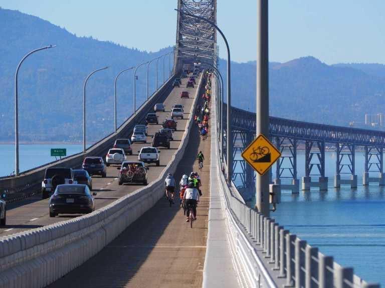 Cars traveling on the Richmond-San Rafael Bridge and bicyclists on the right riding in the bike lane.