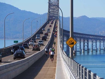 Cars traveling on the Richmond-San Rafael Bridge and bicyclists on the right riding in the bike lane.