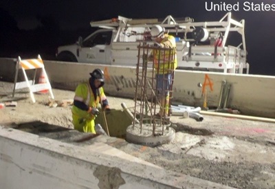 Two Caltrans workers install the base for new lighting in the median of a freeway.