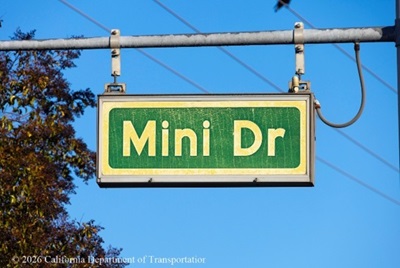 A  green and white street sign for "Mini Dr" hangs from a horizontal bar above State Route 29 in Vallejo, Solano County.