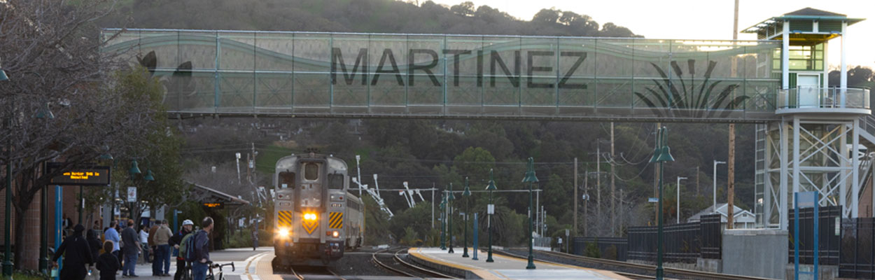 Banner image of Martinez Amtrak station with passengers waiting for the train to stop.