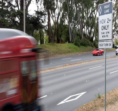 Bus in a HOV bus lane passing a HOV sign.