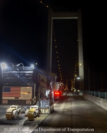 Heavy equipment and trucks are used to remove the roadway surface on the Alfred Zampa Memorial (Carquinez) Bridge on the night of August 21, 2026. The northern bridge tower is visible in the background.