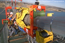 Two workers use a machine to wrap the cable on the Al Zampa span during construction of the western span of the Carquinez Bridge.