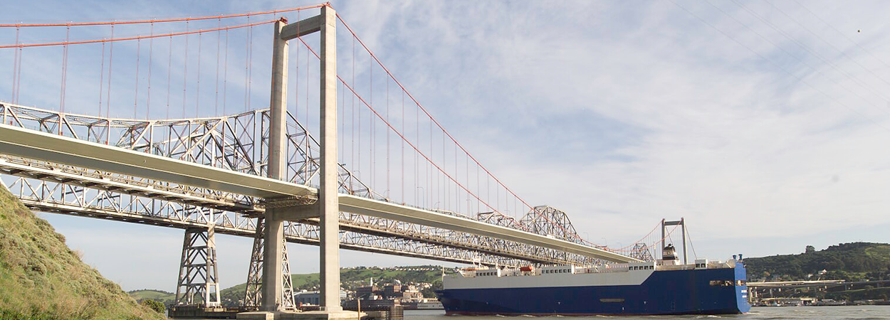 A blue and white ship travels beneath the Carquinez Bridge.