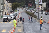 Cars traveling on 19th Avenue (State Route 1) as people cross the intersection while Caltrans is resurfacing the existing asphalt pavement on Southbound 19th Avenue from Lincoln Way to Sloat Boulevard as work continues on the 19th Avenue Paving and Rehabilitation project.