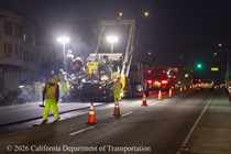 Caltrans uses heavy equipment to apply new pavement to Lane 1 of southbound Highway 1 (19th Avenue) in San Francisco on the evening on May 8, 2026. Traffic continues to flow past the construction in a lane marked with cones.