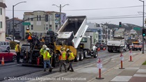 A truck dumps asphalt in front of a paving machine on southbound 19th Avenue (State Route 1) on May 9, 2026.