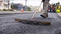 A crewmember uses a long-handled tool during the application of new asphalt on southbound 19th Avenue (State Route 1) as part of the 19th Avenue Paving and Rehabilitation Project on May 10, 2026.
