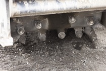 A large metal drum with pointed protrusions attached to heavy equipment which is used to remove old roadway surface material.