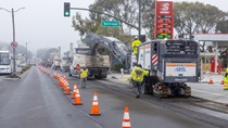 Caltrans uses heavy equipment to remove the old roadway surface and convey it into a truck for removal on southbound 19th Avenue (State Route 1) at Santiago Street on May 10, 2026. The left-hand lane remains open for vehicle traffic and separated from the work area by orange cones..