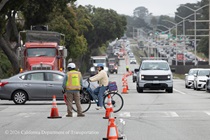 Caltrans crew directing traffic as cars and pedestrians cross an intersection on 19th Avenue (State Route 1) as Caltrans is using heavy equipment to resurface the existing asphalt pavement on Southbound/Northbound 19th Avenue from Sloat Boulevard to Holloway Avenue as work continues on the third of three weekend closures for the 19th Avenue Rehabilitation Project.