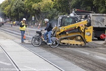 Caltrans worker directing bicyclist to cross the road on 19th Avenue (State Route 1) as Caltrans is using heavy equipment to resurface the existing asphalt pavement on Southbound/Northbound 19th Avenue from Sloat Boulevard to Holloway Avenue as work continues on the third of three weekend closures for the 19th Avenue Rehabilitation Project.