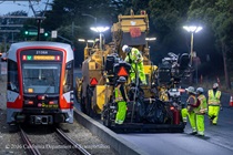 Caltrans crew using heavy equipment to prepare and resurface the existing asphalt pavement as a Muni train passes by on Southbound/Northbound 19th Avenue from Sloat Boulevard to Holloway Avenue as work continues on the third of three weekend closures for the 19th Avenue Rehabilitation Project.