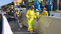 Crew members in high visibility clothing perform finishing work on the fresh concrete of the new median barrier install on US 101 in San Francisco.