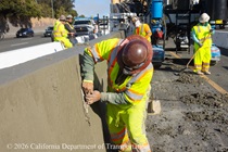 A crew member performs finishing work on the fresh concrete for the new median barrier on US 101 in San Francisco.