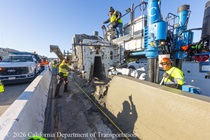 Caltrans crew using slipform paver and a crew member is doing finishing work on fresh concrete for the new median barrier as part of the US 101 Hospital Curve Rehabilitation Project on March 28, 2026.