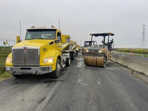 Trucks and a roller vehicle are on State Route 37 as part of a Caltrans paving project.