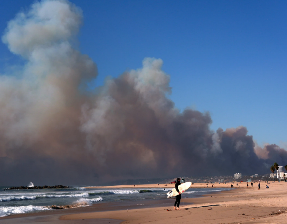 Surfer on the beach looking at a cloud of smoke rising from the Los Angeles wild fires.