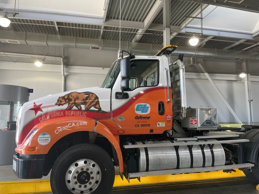 An orange and white truck features a Caltrans logo on the door and the bear and star from the California flag featured above the front wheel.
