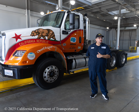 A CHP worker in blue coveralls stands in front of an orange and white truck.
