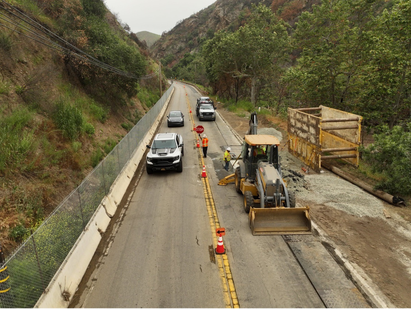 Cars driving on one lane of Topanga Canyon Boulevard/State Route 27, with workers in hi-vis apparel seen holding a stop sign and working in a closed lane.