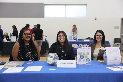 Three Caltrans staff members seated at an exhibit table at a small business outreach event