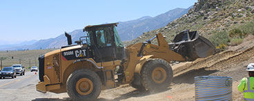 An earthmover working on a Caltrans project. A project monitor stands in the foreground on the right.