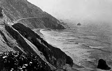 Black and white image of sloping coastline with a highway winding along it.