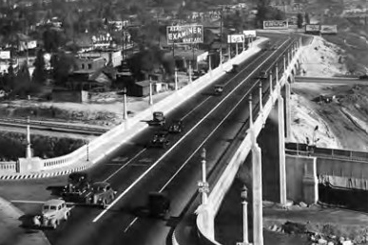 1940s era cars driving across a 4 lane concrete bridge.