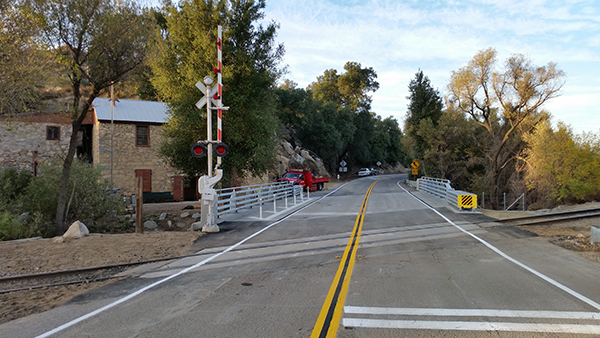 View of a highway extending off into the distance. A section of the highway has a railroad crossing followed by a railing on either side of the road with vegetation.