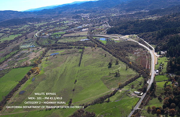 From above, a view of a highway winding around a rural area with wetlands.