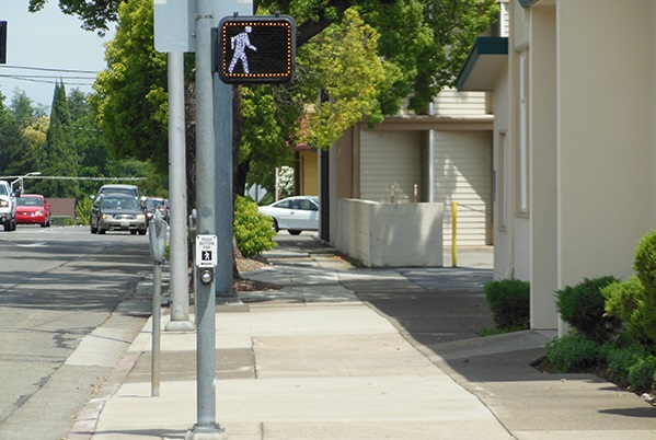 A street corner with a pedestrian signal walk sign with a yellow LED border.