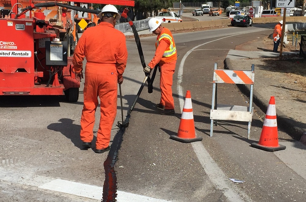 Construction workers poring and evening out a construction material onto the surface of the highway.