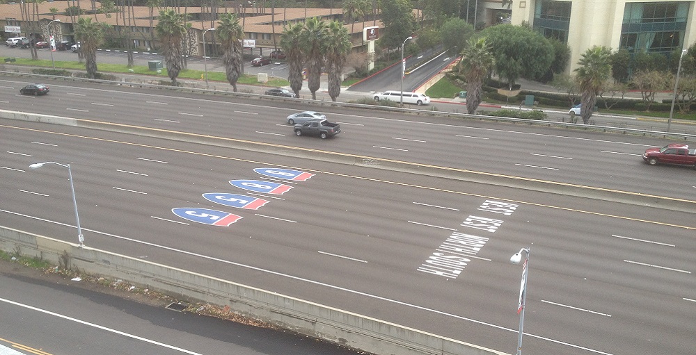 View from above of a multi-lane freeway with painted icons of upcoming turnoffs.