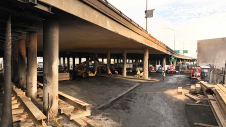 Photo of ongoing repair work on Interstate 10 freeway in Downtown Los Angeles from another angle showing workers building wooden "shoring" framework to support damaged infrastructure from a Nov 11, 2023 fire. 