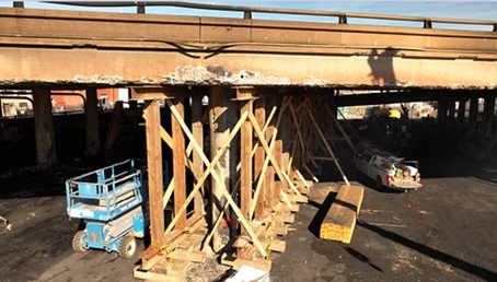 Photo of ongoing repair work on Interstate 10 freeway in Downtown Los Angeles showing workers building wooden "shoring" framework to support damaged infrastructure from a Nov 11, 2023 fire. 