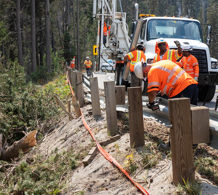 Photo of Caltrans workers repairing guardrail along a forested highway.