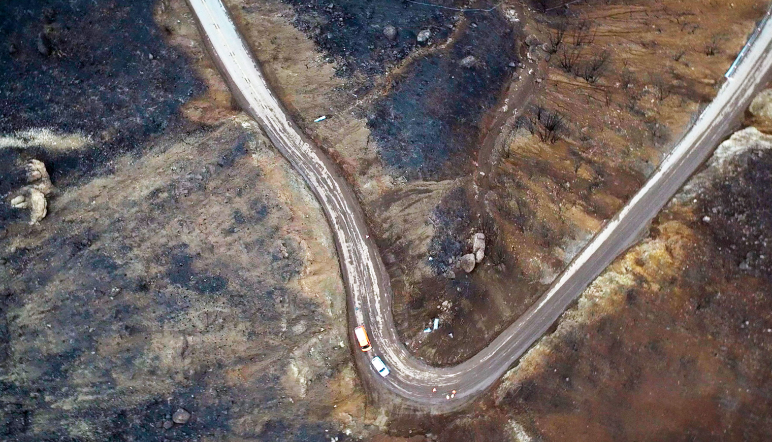 Aerial view of a highway winding through burn-scarred terrain in southern California.