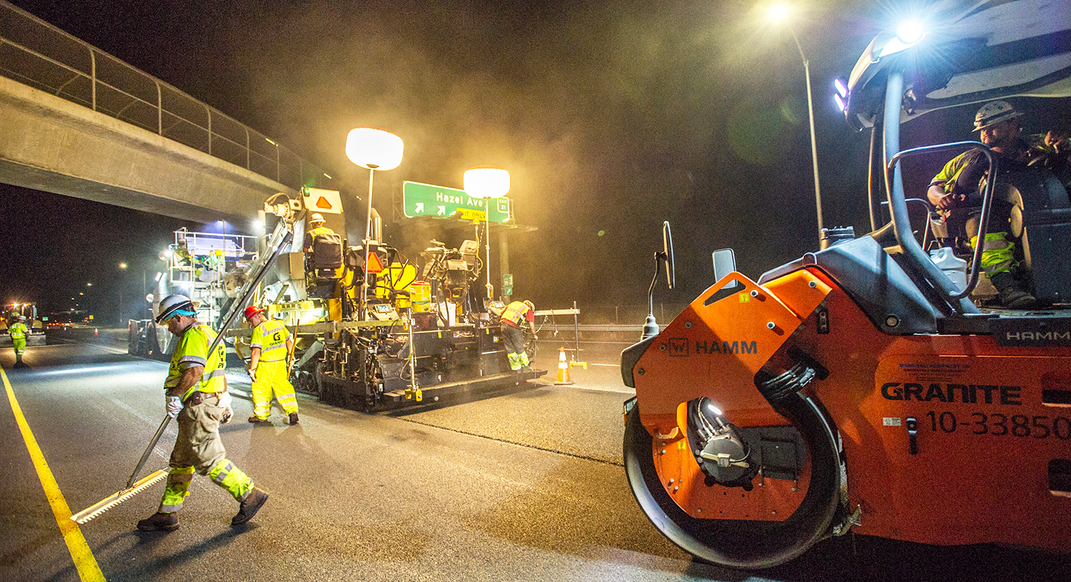 Photo of a paving machine and crew repairing pavement at night