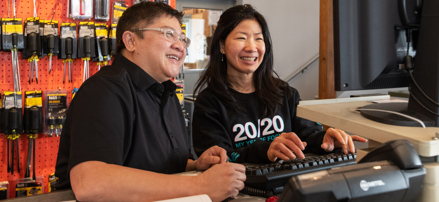 A business owner and employee are smiling as they go over figures together in front of a computer screen.
