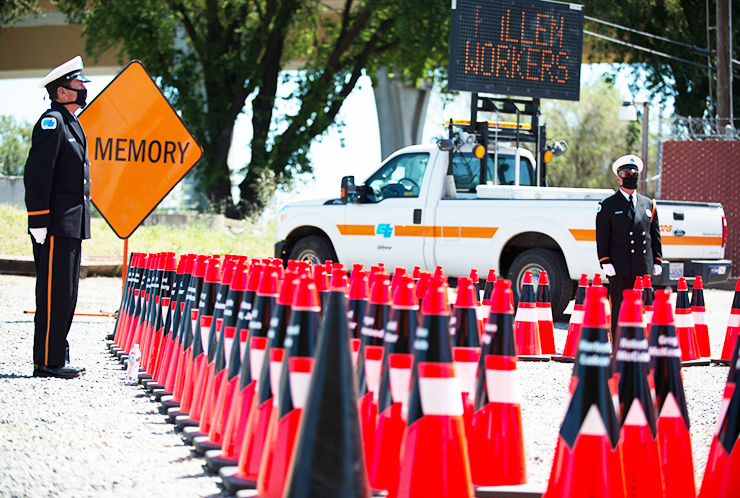 Two Caltrans honor guards stand vigil with memorial cones and Caltrans vehicle in the background during the 2020 Workers Memorial.
