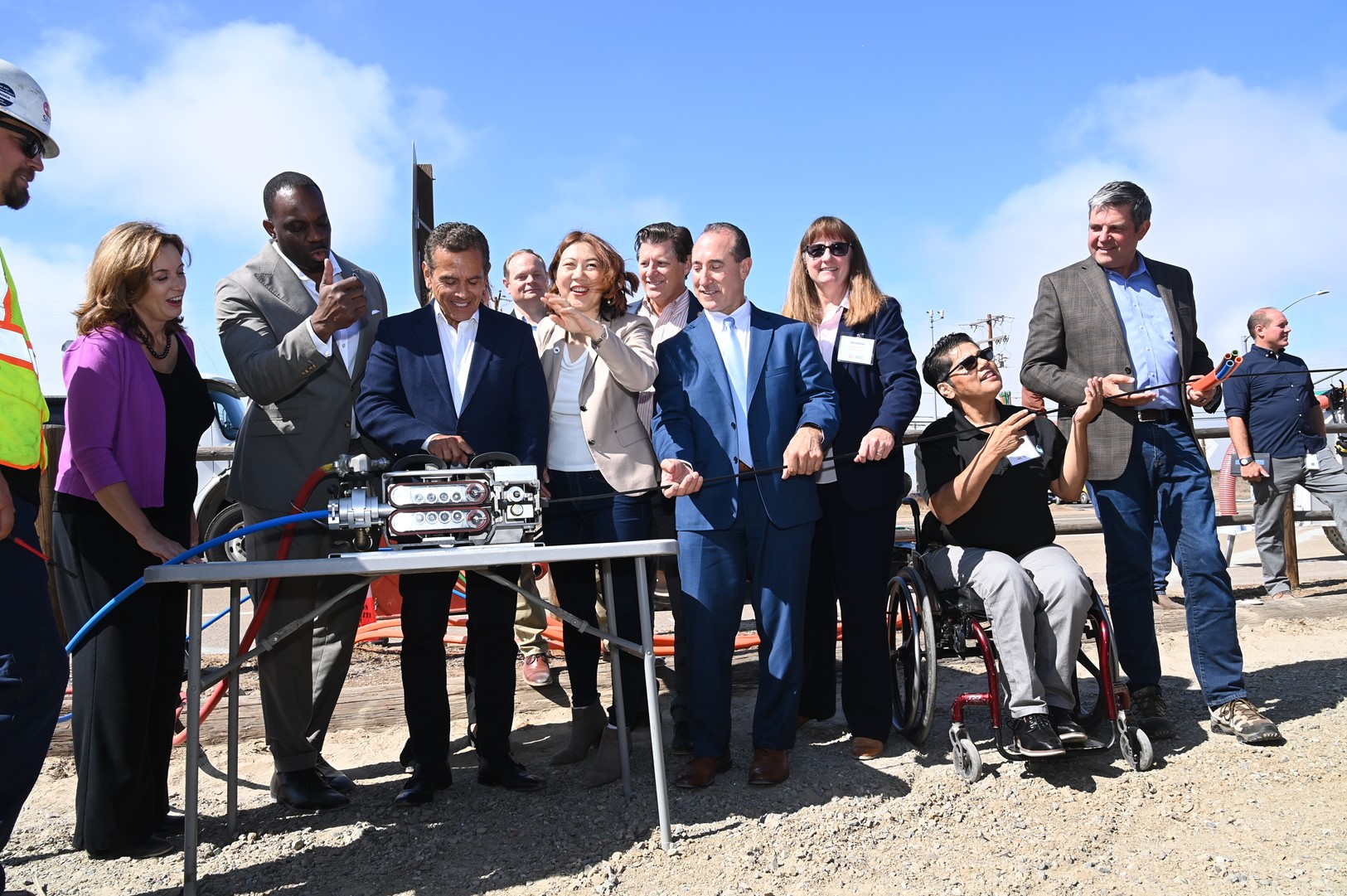 A group photo of people, including California leaders such as California Transportation Secretary Toks Omishakin and Caltrans Director Tony Tavares, watch former Los Angeles Mayor Antonio Villaraigosa kick off the start of construction by flipping a switch to insert the first fiber cable into the ground, representing the first of 10,000 miles of high-speed broadband internet that will be integrated into California's infrastructure.