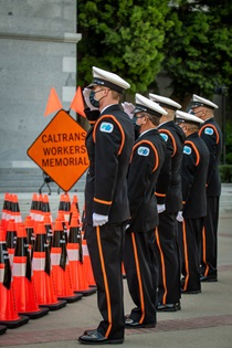 Caltrans Honor Guard members salute with an orange "Caltrans Workers Memorial" sign in the background - 31st Annual Caltrans Workers Memorial Ceremony April 29, 2021 - California State Capitol, Sacramento
