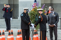 Caltrans Honor Guard members place a ceremonial wreath that reads "In Loving Memory Of" accompanied by a bugler; a member of the Caltrans Choir and Caltrans Director Toks Omishakin are visible in the background - 31st Annual Caltrans Workers Memorial Ceremony April 29, 2021 - California State Capitol, Sacramento