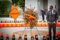 Caltrans Director Toks Omishakin stands among 189 orange cones that each bear the name of a fallen Caltrans worker to honor their sacrifices. An orange "In Memory" sign, a ceremonial "In Loving Memory" floral wreath and a bugler complete the scene - 31st Annual Caltrans Workers Memorial Ceremony April 29, 2021 - California State Capitol, Sacramento