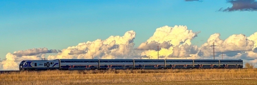 Amtrak running through a field with a sky and clouds in the back