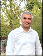 The picture is a portrait of Madhi Khorram a transportation engineer who was killed serving California in September 2025. Madhi is wearing a white shirt and there are green trees in the background.