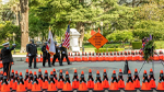 Caltrans honor guard members saluting US and California flags during the 2021 Caltrans Workers Memorial ceremony in Sacramento; California's Capitol Park to honor fallen highway workers. They are surrounded by orange cones wrapped in black bands with the names of each of the 189 fallen workers. The cones are arranged in the shape of a diamond; mimicking the orange "Slow for the Cone Zone" sign in the middle.